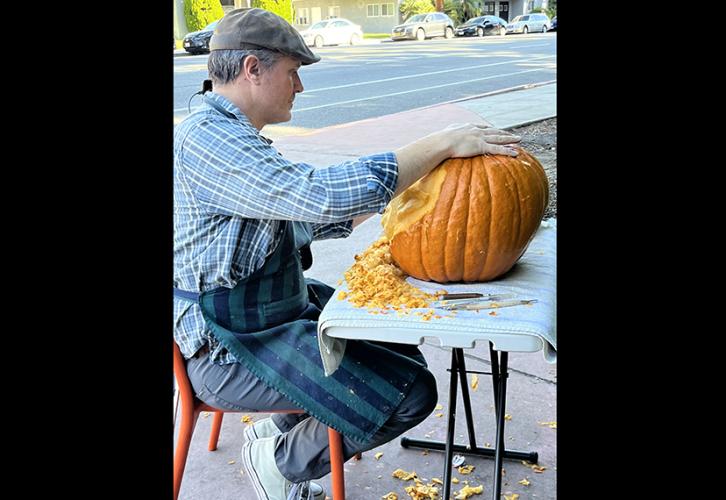 McHugh sits at a table set up on the sidewalk carving a pumpkin.