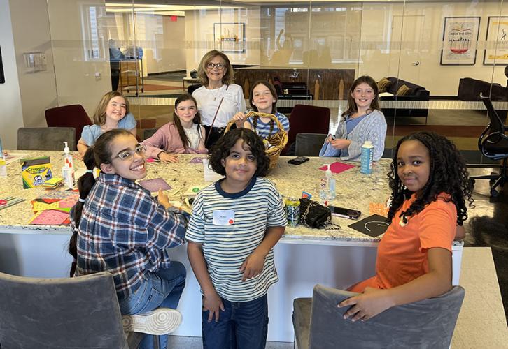 People sit around a long tan table with arts and crafts supplies in front of them.