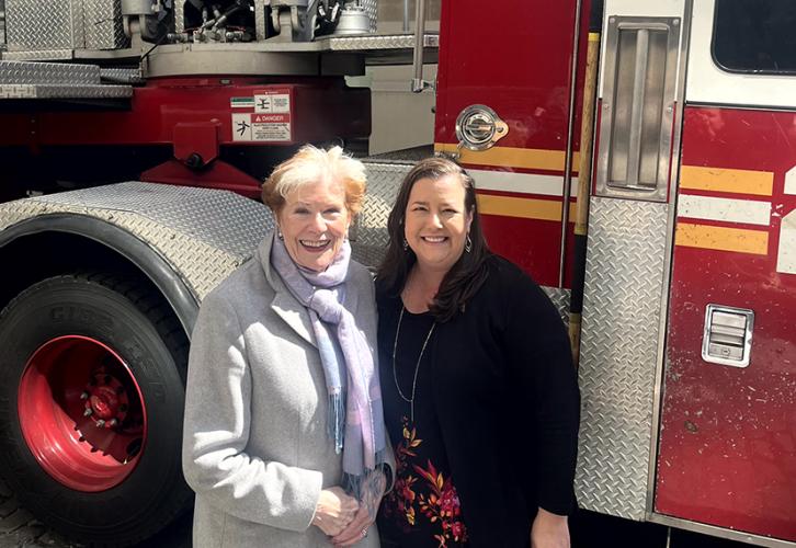 Two people smile in front of a fire truck.