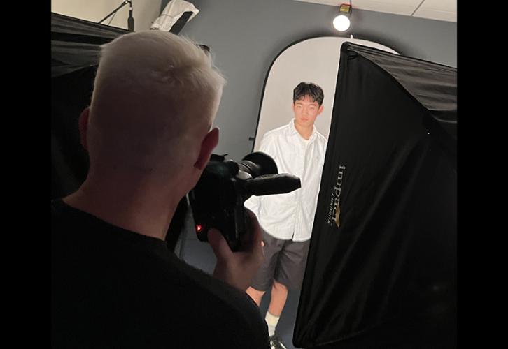 A photographer with his back to the camera takes photos of an actor against a gray backdrop.