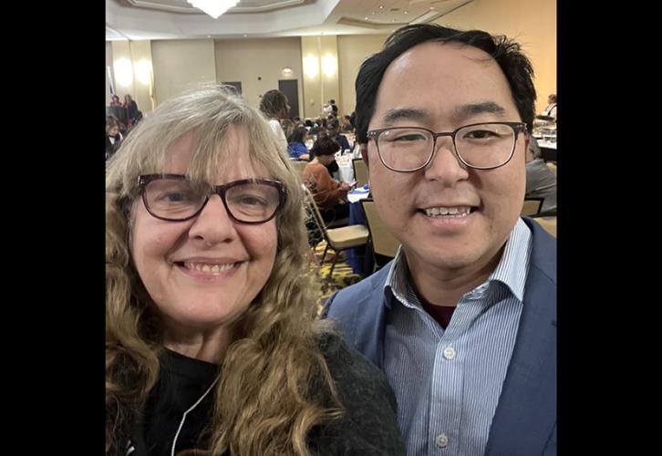 Closeup of two people smiling in a large room.