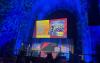 On a projector screen onstage, a photo from the 2023 strike appears. Beside the photo reads the copy, “Winner SAG-AFTRA 2023 Negotiations and Strike Campaign Winner” in white. Some other equipment and SABRE Award regalia are visible.