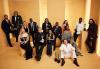 The cast of The Bear pose in a yellow room with their award statuettes. Some are seated and some are standing.