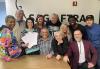 New England Members smile and bond after an intensive Cold Read workshop. A group of people gather around a table, in front of a wall painted with the SAG-AFTRA logo.