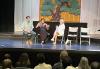 Panelists Eric Johnson, Aubrey Staley and Rachel Whitley discuss the business of acting in Hawaii. Three people, one man in an aloha shirt, one woman in a black sundress, and a woman in a white shirt dress, sit on a well-lit stage before an audience of actors. There is a backdrop with an illustration of a bonsai tree.