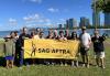 Top photo: Members hold a SAG-AFTRA banner and enjoy each other’s company under the blue Hawaiian skies. A group of 14 members and families made up of Hawaiian, Asian and white people stand on a grassy picnic area holding a large yellow banner. The banner has the black performer logo and black letters spelling out “SAG-AFTRA.”