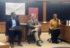 Harvard Law student Brandon McCoy, left, moderated the panel for the “Harvard Journal on Sports and Entertainment Law.” McCoy was joined by Minnesota Law professor Matthew T. Bodie, center, and Local President Andrea Lyman. The three are seated. McCoy, in a dark suit, holds a laptop computer; Brodie, in a gray suit, sits with his legs crossed; Lyman, in a yellow sweater and black pants, speaks into a microphone.