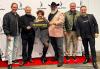 Six people stand on a red carpet in front of a banner with the SAG-AFTRA logo on it, smiling and holding a #SagAwards sign.