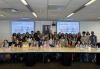 A diverse group of people smile in front of a long tan table. Two screens that read Kids and Teens Day at the Sag-Aftra Foundation are on either side of them.
