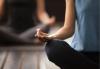 Performing at Your Best Female seated cross-legged in a blue tank top and dark grey yoga pants with the back of her right hand resting on her right knee. Pinky, ring and middle finger pointing forward with her index and thumb touching to form a circle