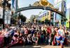 Members and friends pose under the Gaslamp Quarter arch. A large group of people pose for a photo on a street under an arch that reads “Gaslamp Quarter: Historic Heart of San Diego.” Some of the people wear SAG-AFTRA T-shirts and many are wearing costumes, including Superman, Spiderman and others.