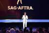 SAG-AFTRA President Gabrielle Carteris Carteris in white suite on a stage speaking into a mic looking out at the audience