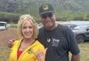 Hawaii Local Board member Sally Davis with Brian Keaulana. On the left, a person wearing a yellow sweatshirt throws a shaka. On the right is a person in a black T-shirt and black baseball cap.