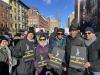 SAG-AFTRA members show their support for the Atlantic Theater workers. From left, Judith Ackerman, New York Local Board member Marc Baron, Dani Carr, New York Local Board member Avis Boone, New York Local President Ezra Knight, and Robert Jimenez. A group of diverse people dressed in winter coats hold black signs that read “SAG-AFTRA in Solidarity” in white and yellow text