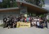 A large, diverse group outside in a park. Many wear black SAG-AFTRA T-shirts. In the center front row, some hold a large yellow banner with the SAG-AFTRA logo.