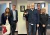 Six close family members of John Henning pose for a photo next to the plaque in the New England Local boardroom officially honoring his legacy, four on the right side and two on the left. 