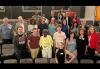 After participating in a mock audition workshop, Nevada Local members and casting director Jordan Bass gather for a group photo. A diverse group of people pose for a photo among the seats in a theater. Most of the people wear casual clothing and a nametag.