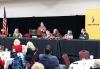 Kim Spurgeon, Director, Nevada Film Office educates members about Nevada Film Tax Incentives bills. Photo by Denise Vasquez Photography. A person stands at a podium speaking, while six others sit on the dais on either side. People sitting at round tables listen to the speaker.