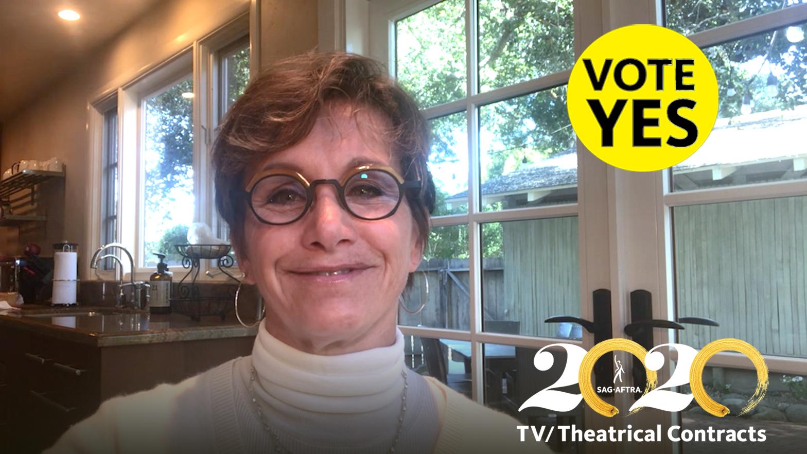 Vote Yes Carteris in white turtle neck and circle glasses in front of windows with a yellow "Vote YES" with black text in the top right corner and 2020 TV/Theatrical logo in bottom right corner